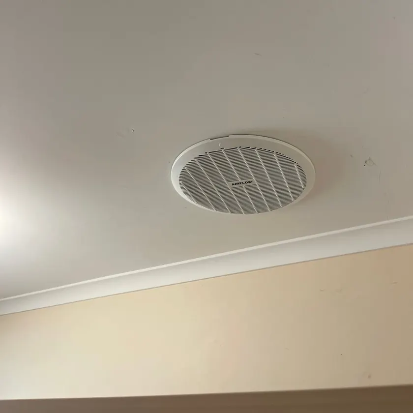 Round white exhaust fan grille fitted in a ceiling near the cornice