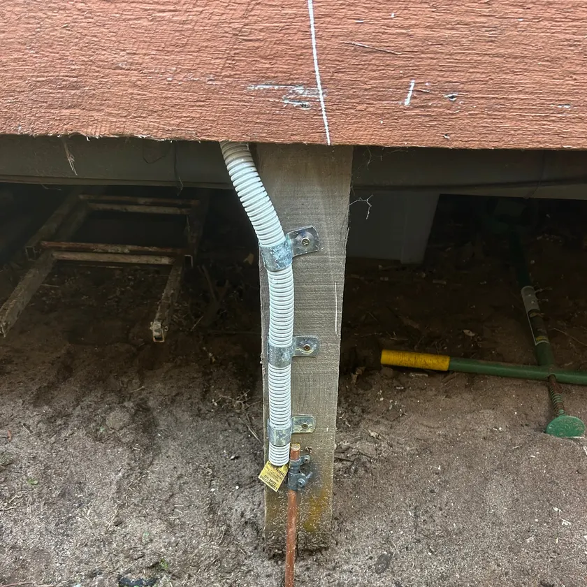 Grey flexible conduit clipped neatly down a timber stump to a new copper earth stake in the ground