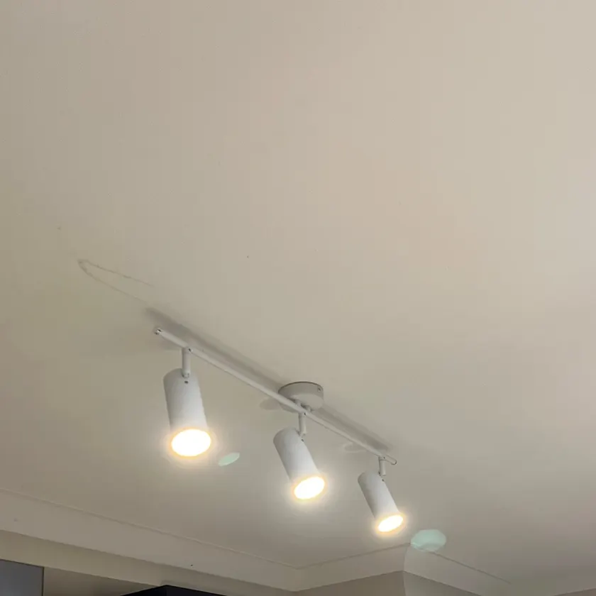 White three-spot track light switched on, mounted on a kitchen ceiling