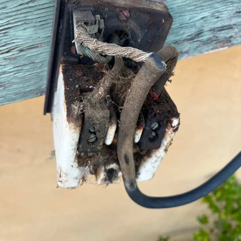 Old deteriorated service fuse and frayed mains cable on a weathered fascia