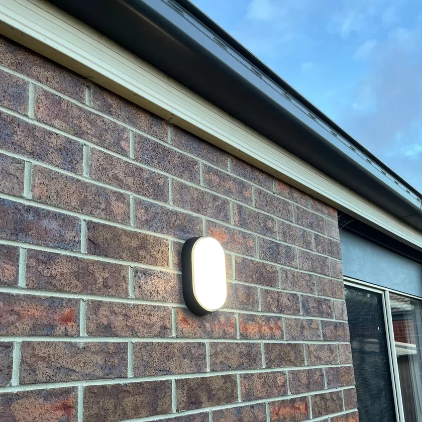 Oval bunker-style outdoor light switched on, mounted on a brick wall