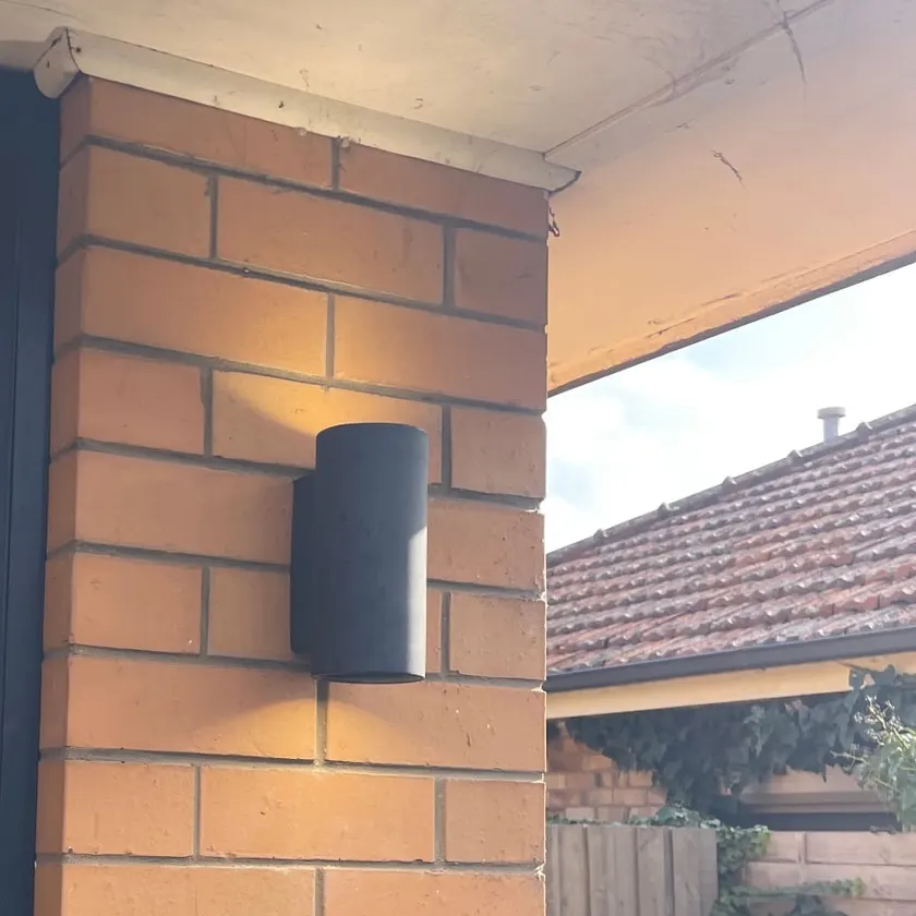 Black up-and-down wall light mounted on an exterior brick pillar