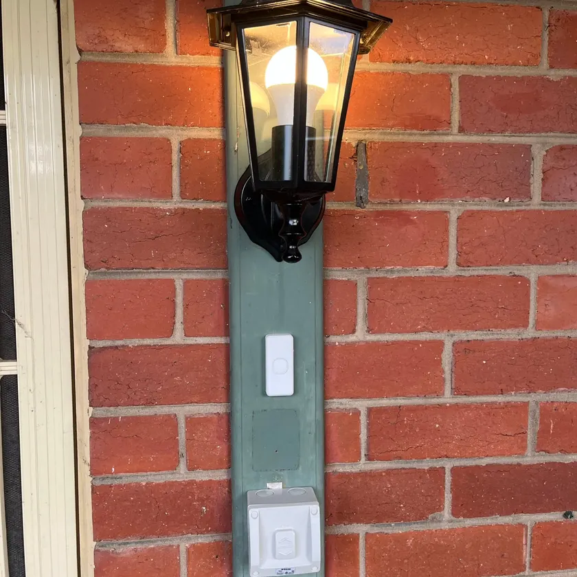 Lit coach lantern on brick with a doorbell push and a weatherproof switch