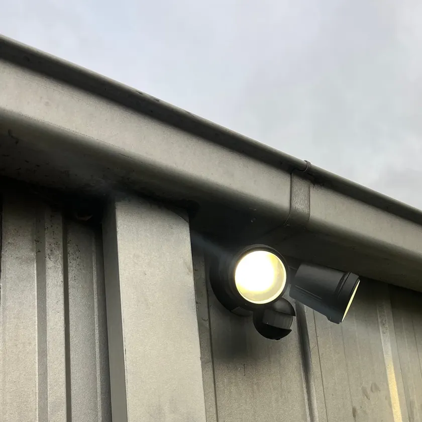 Twin sensor floodlights on a steel shed wall