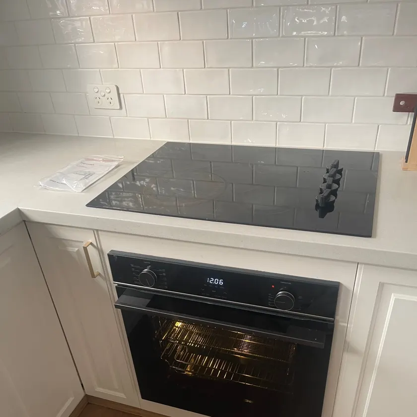 Black built-in oven with its light on beneath a ceramic cooktop in a white kitchen