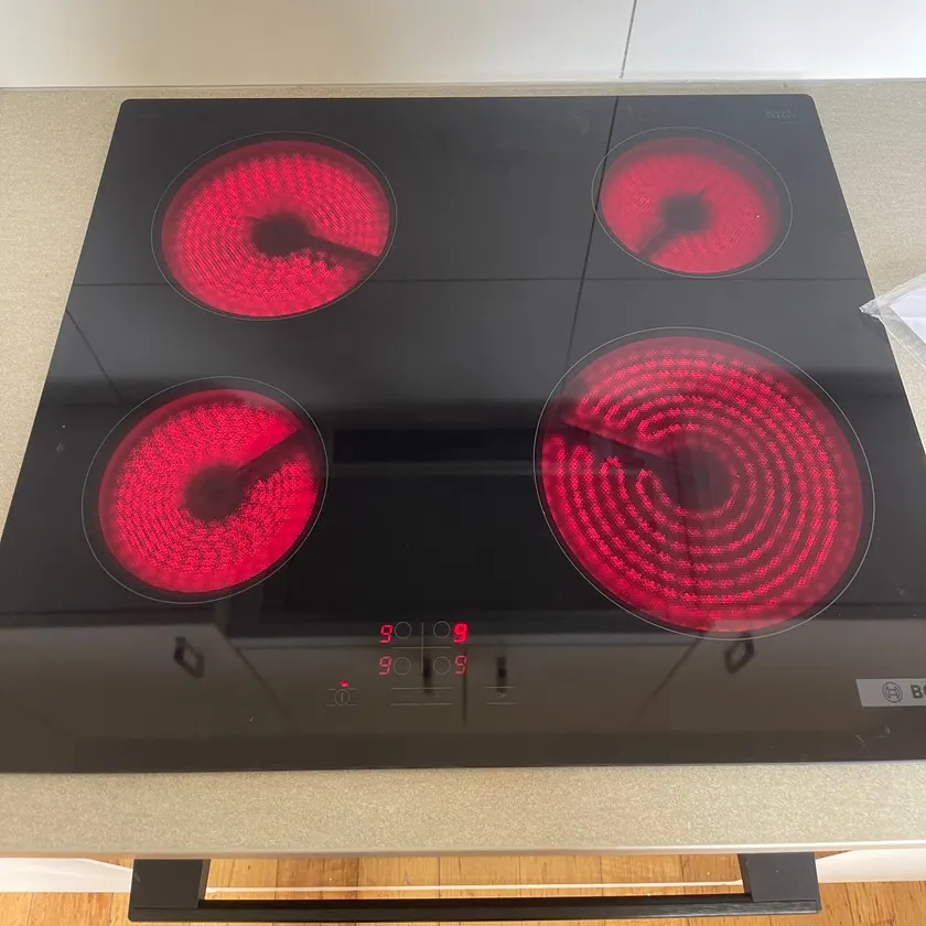 Black ceramic cooktop with all four elements glowing red during testing