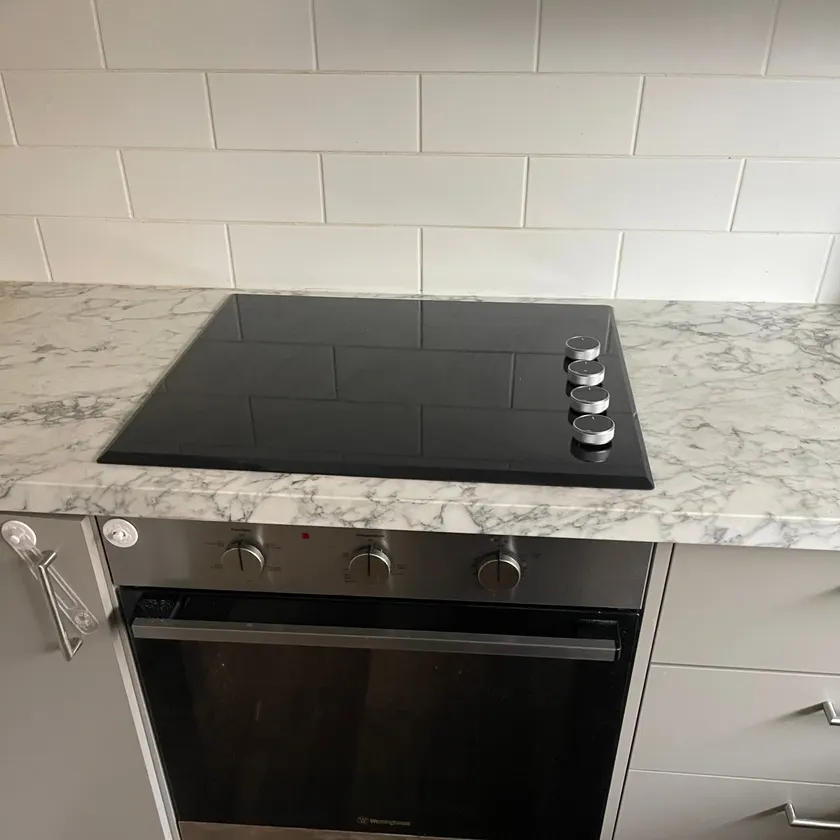 Stainless under-bench oven below a black ceramic cooktop set in a marble-look benchtop