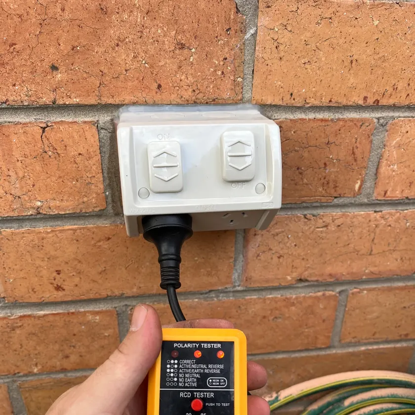 Weatherproof double outdoor power point on a brick wall with a polarity and safety switch tester plugged in