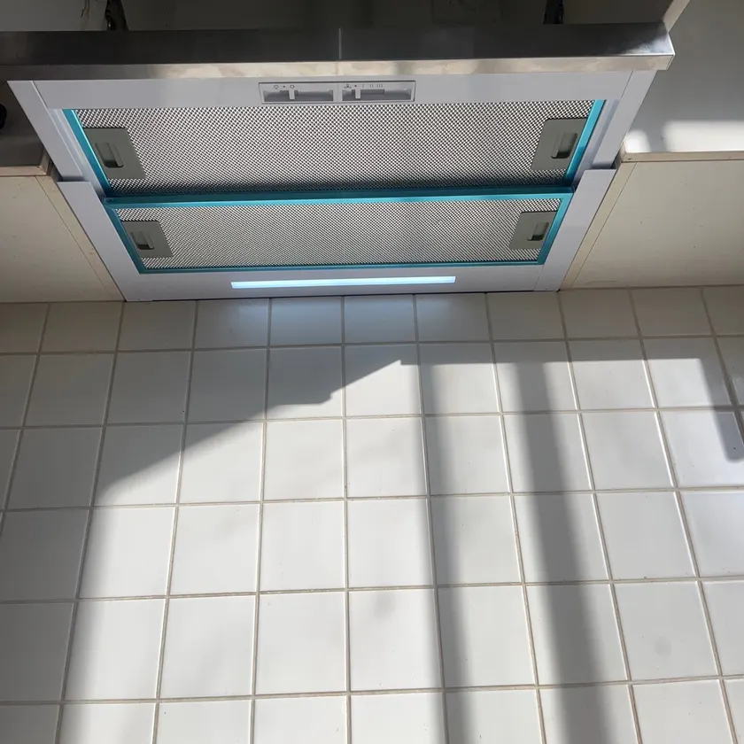 Slide-out rangehood seen from below with its light on and protective film on the filters