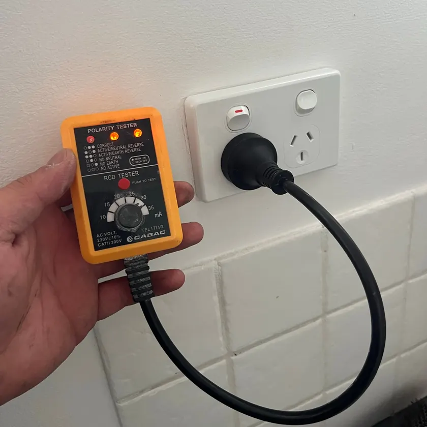 Hand holding a plug-in polarity and safety switch tester at a double power point