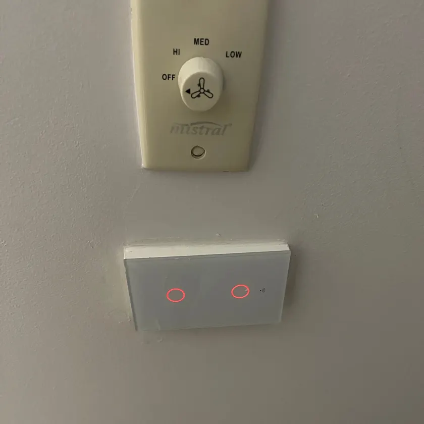 Two-gang smart touch switch panel with glowing indicator rings mounted on a wall below a fan speed control