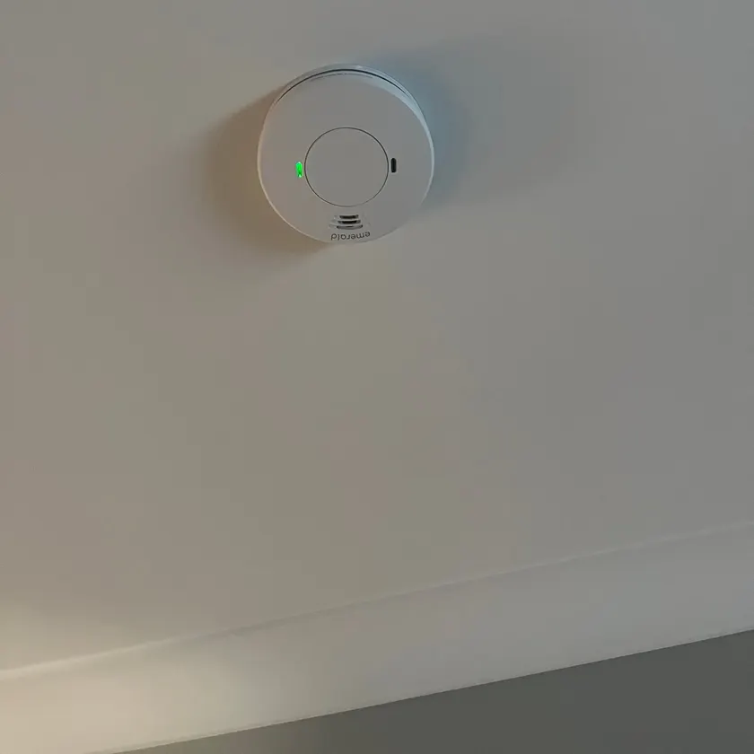 White smoke alarm mounted on a ceiling with a green mains power light showing
