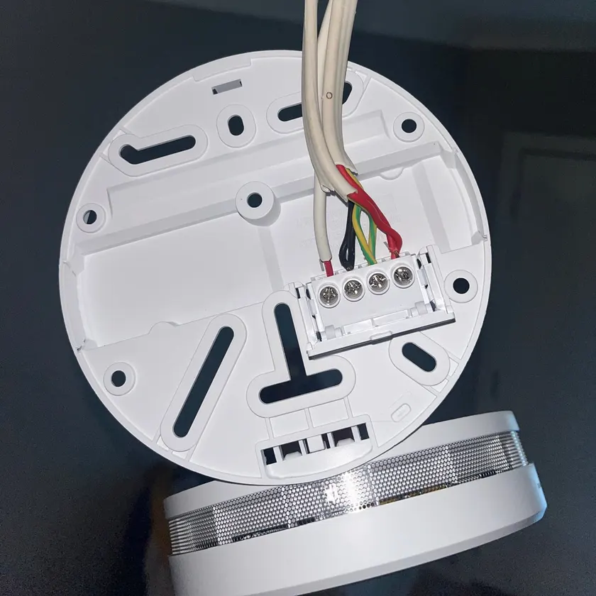 Smoke alarm mounting base with mains cables terminated in its four-way connector block before the alarm is fitted