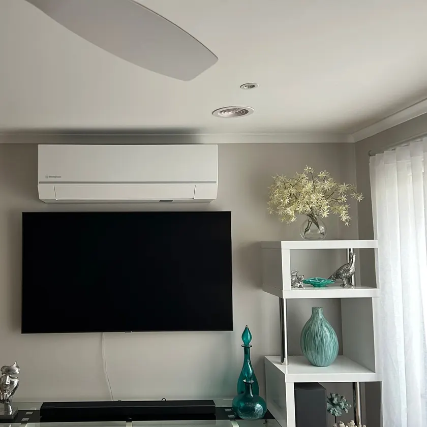 Large television wall-mounted below a split system in a styled living room, screen off