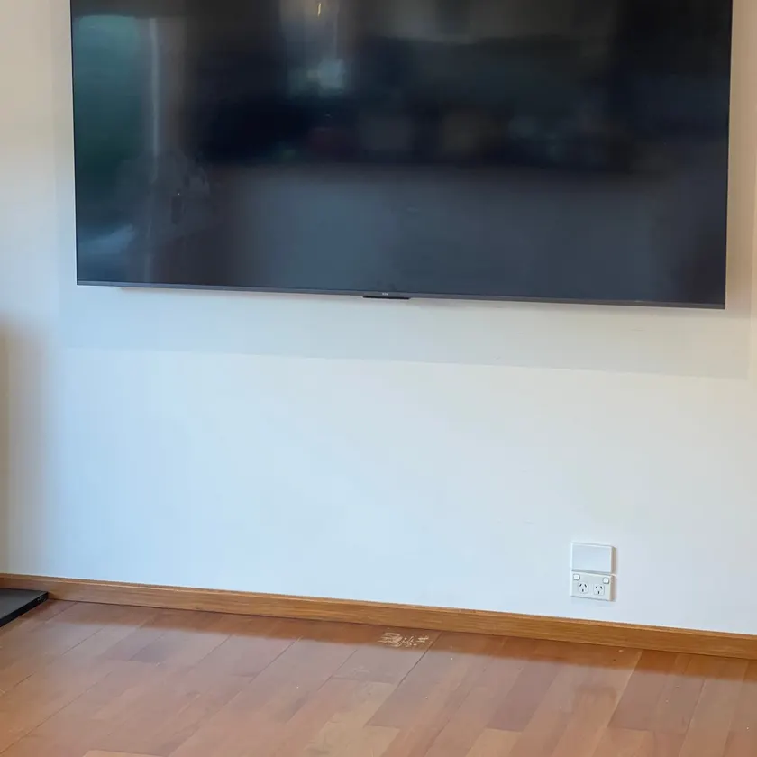 Large television mounted flat on a plain wall with no cables showing, screen off