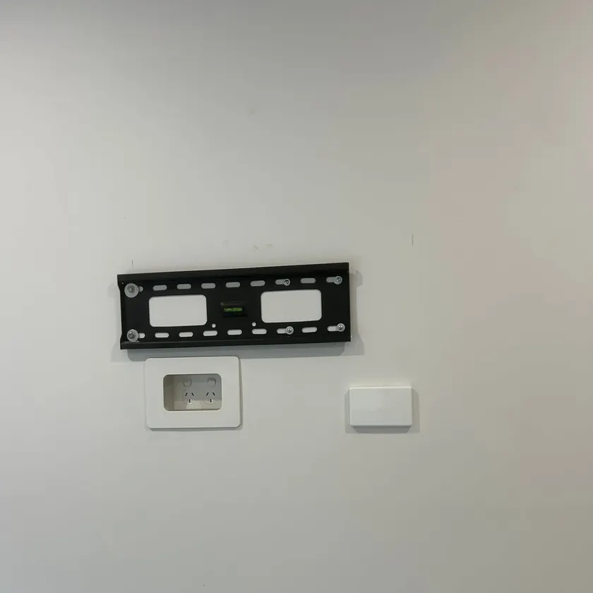Black TV wall bracket with a recessed double power point and blank plate beneath it