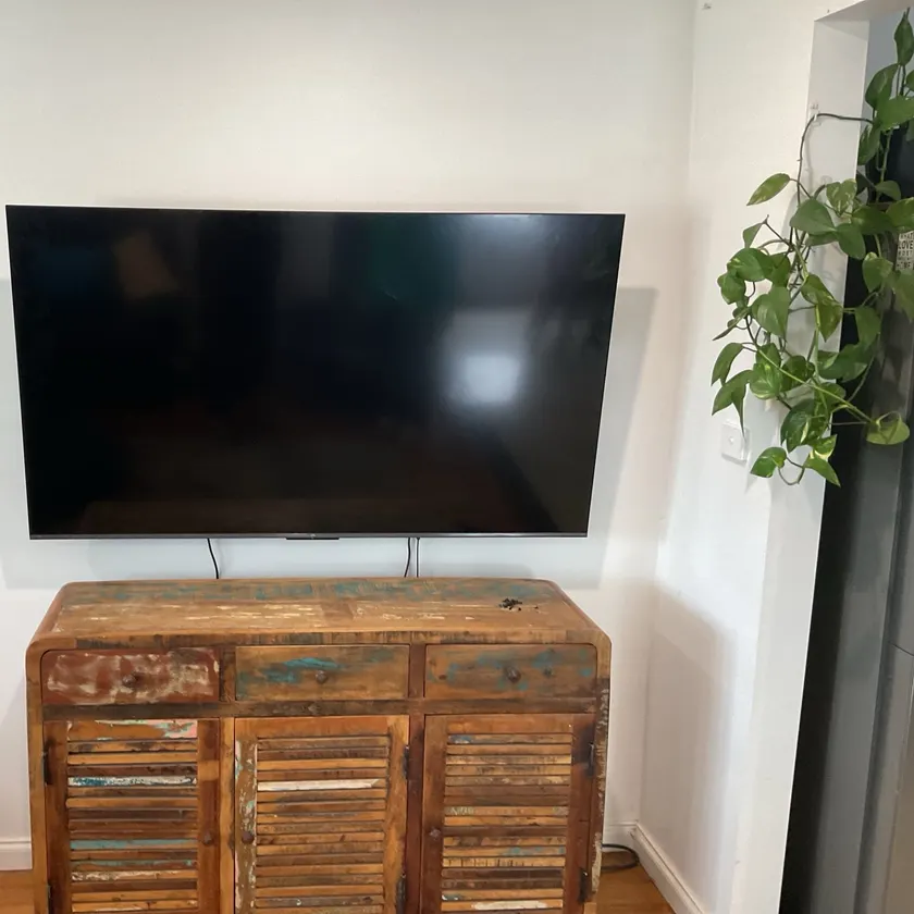 Television mounted on a white wall above a timber sideboard, screen off