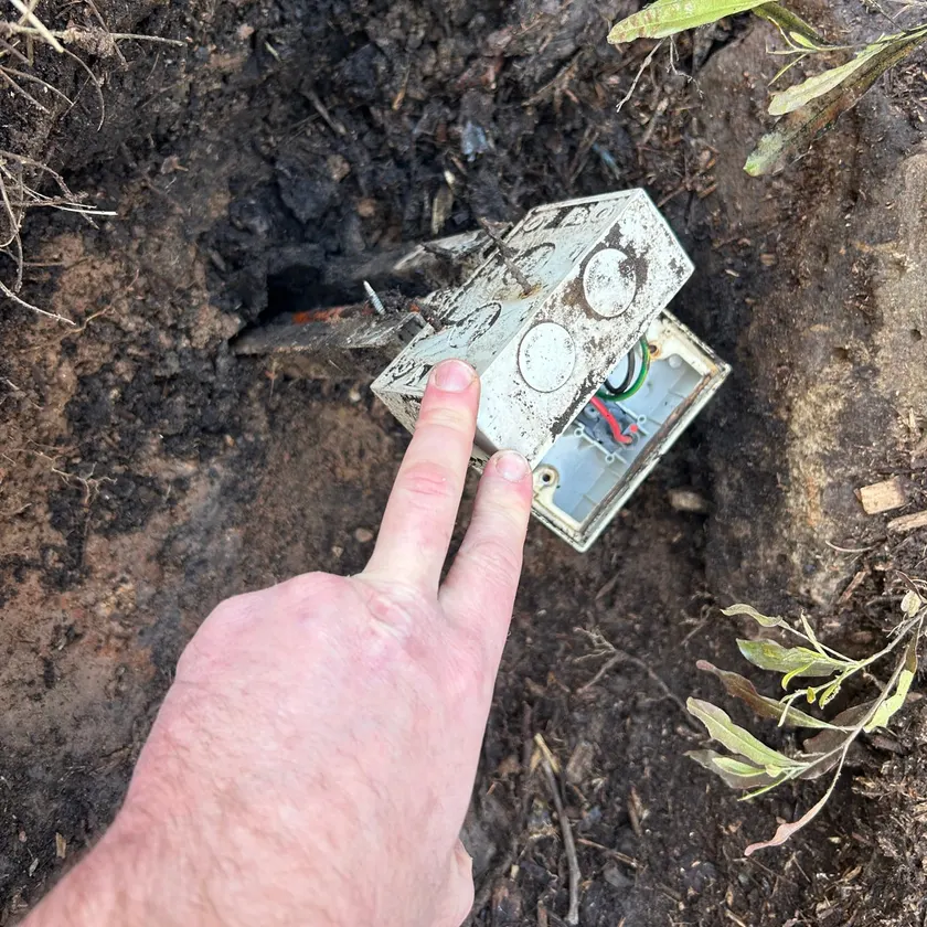 Hand pointing at an old junction box found buried in garden soil