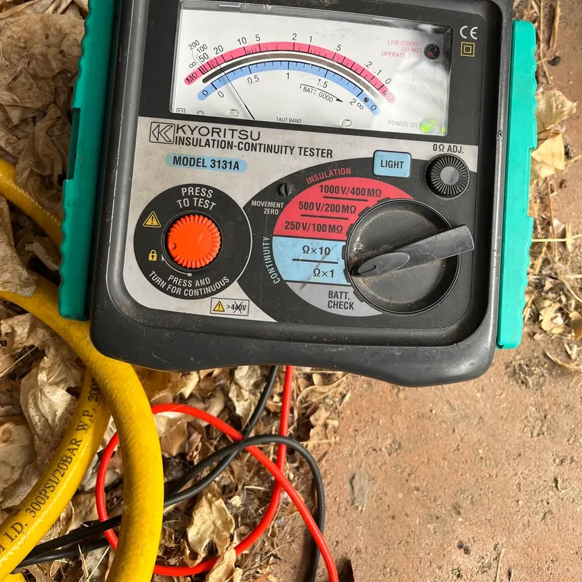 Insulation and continuity tester with test leads, resting on dry leaves outdoors
