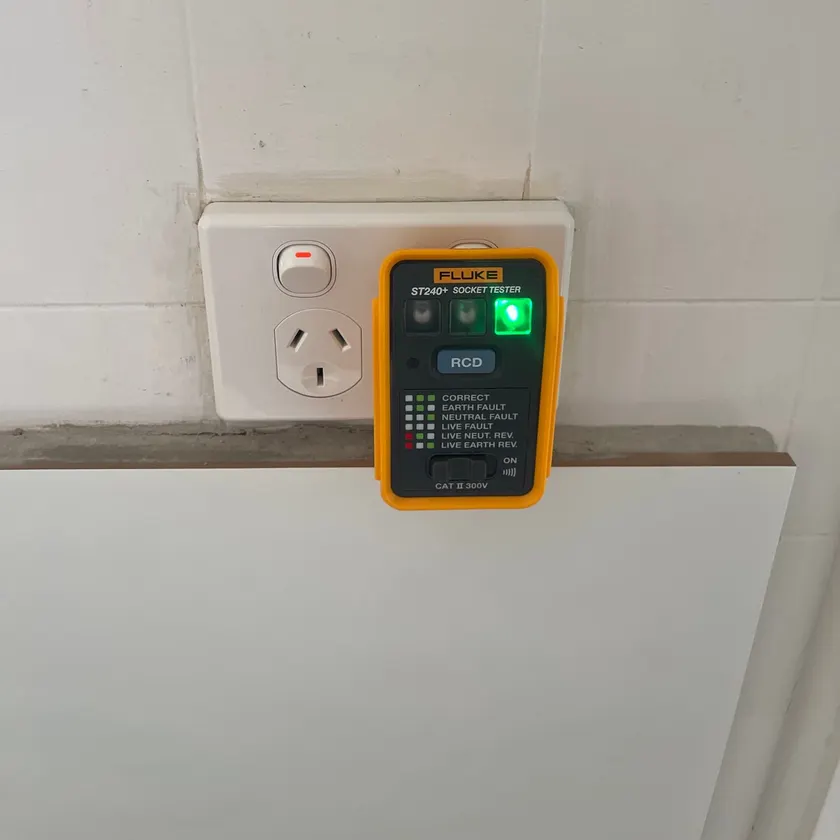 Socket tester plugged into a new double power point on a tiled wall, showing a green correct-wiring light